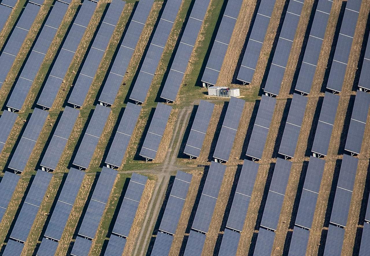 Aerial view of rows of solar panels across a field, with a small equipment building at one edge